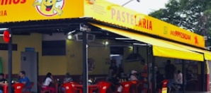 Fachada amarela da pastelaria com as mesas vermelhas na calçada